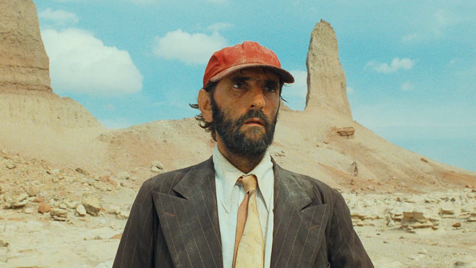 Mann mit roter Baseballmütze und Anzug in einer Wüstenlandschaft