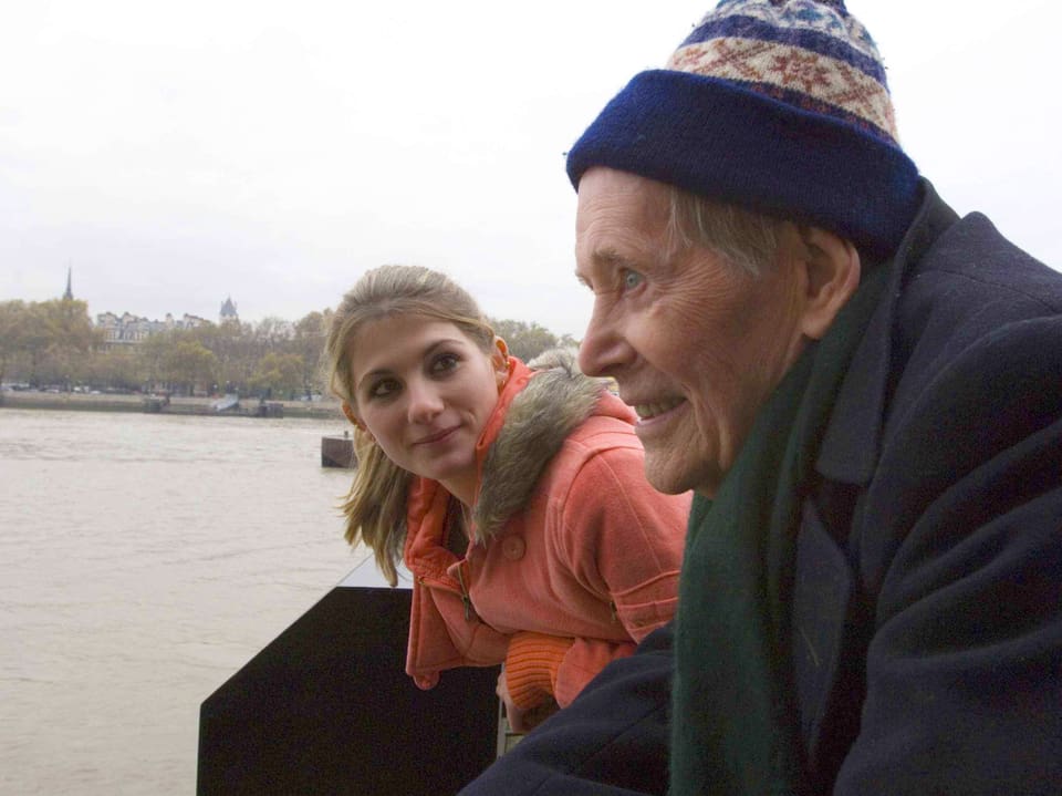 Alter Mann und junge Frau im Gespräch an einem Fluss.