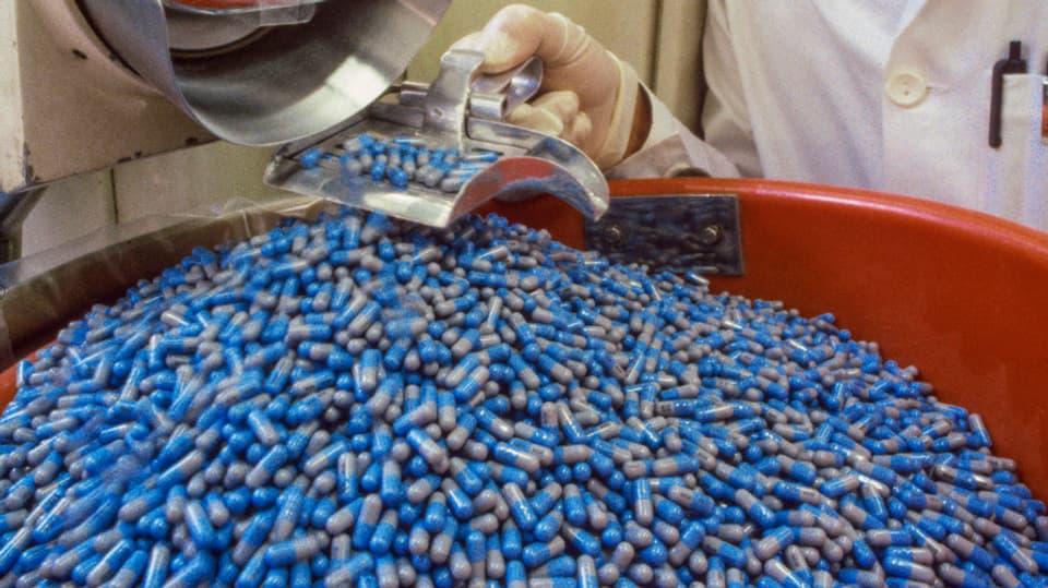 Blaue Pillen purzeln aus einer Maschine in ein tonfarbenes Gefäss