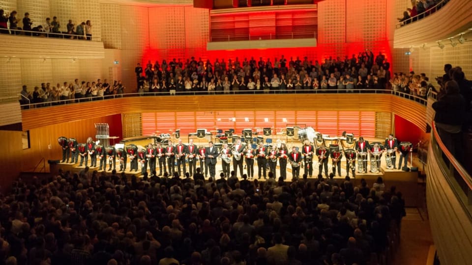 Eine Brass-Band auf der Bühne eines festlichen Konzertlokals.