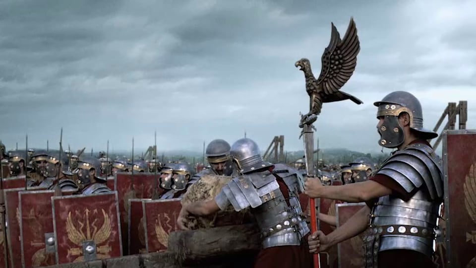 Römische Soldaten auf einem Schlachtfeld, zwei Männer laden ein Katapult.