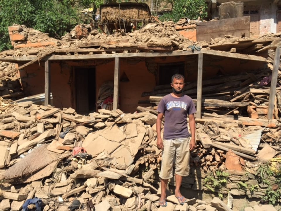 Ein Mann vor den Trümmern eines halb eingestürzten Hauses.