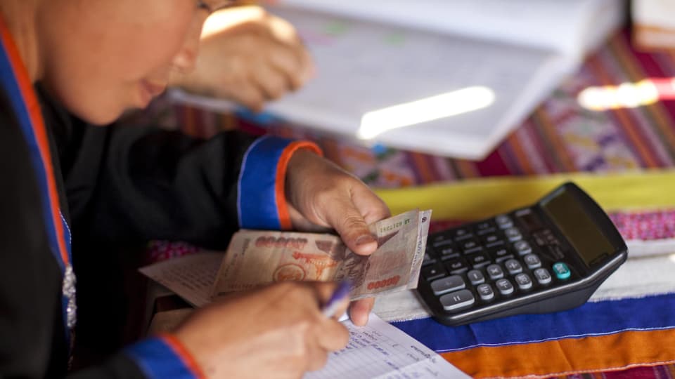 Asiatisches Mädchen zählt Geld vor Taschenrechner