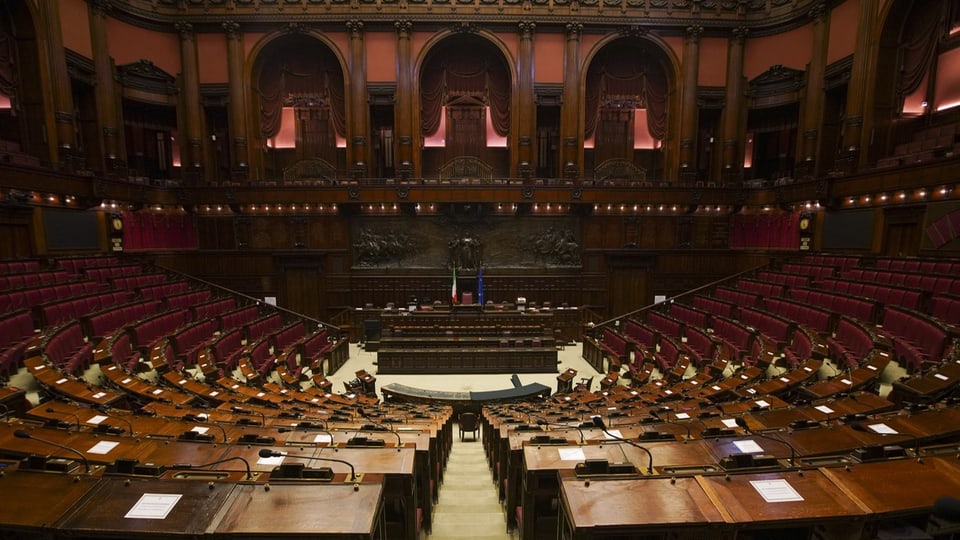 Leerer Plenarsaal des italienisches Parlaments mit Holzsitzen und zentralem Rednerpult.