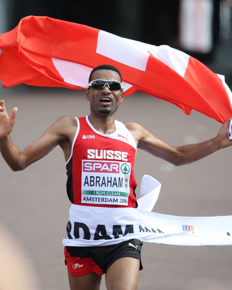 Tadesse Abraham läuft mit Schweizer Flagge ins Ziel.