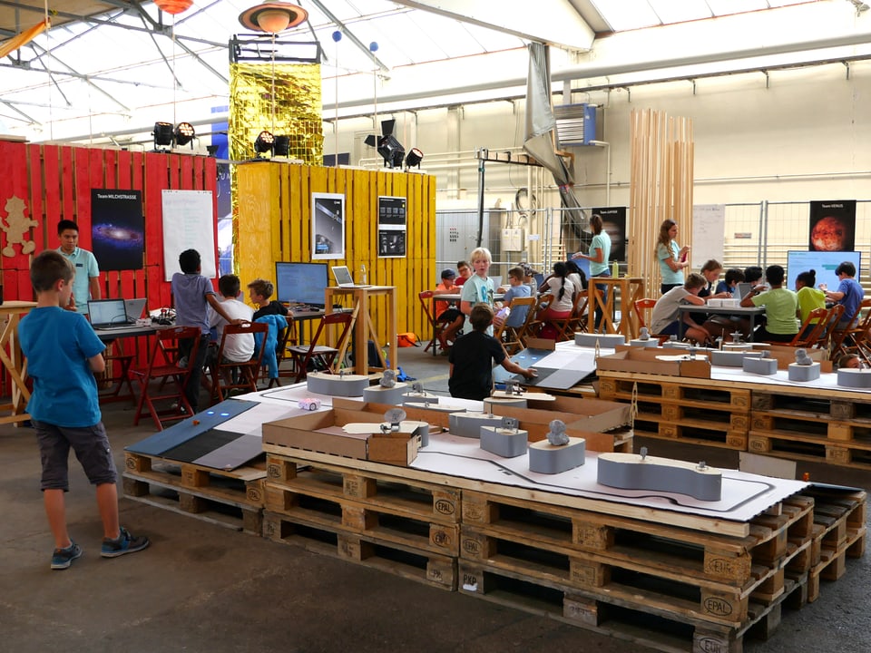 In einem Flugzeughangar sind auf Holzpaletten Hindernisparcours für die Raumfahrt-Roboter der Kinder aufgebaut.