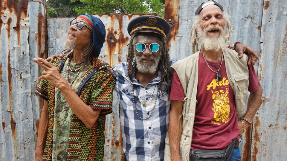 Drei Reggae-Musiker vor einem zaun.