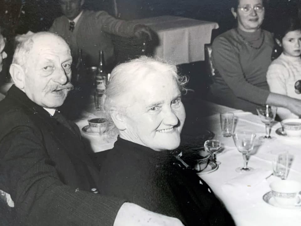 Eine ältere Frau und ein Mann sitzen lachend an einem Tisch.