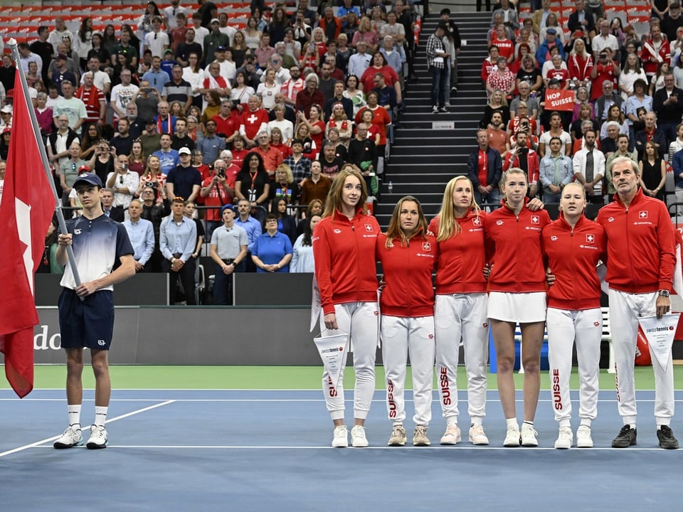 Tennismannschaft der Schweiz bei einer Zeremonie auf dem Tennisplatz, vor einem Publikum.
