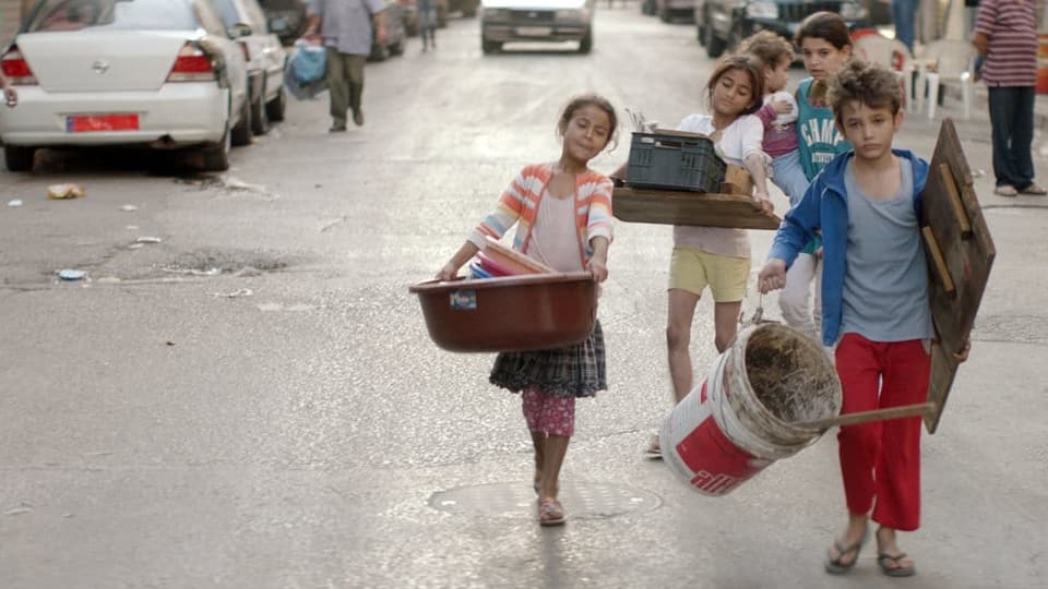 Vier Kinder tragen Baumaterial durch eine Strasse.