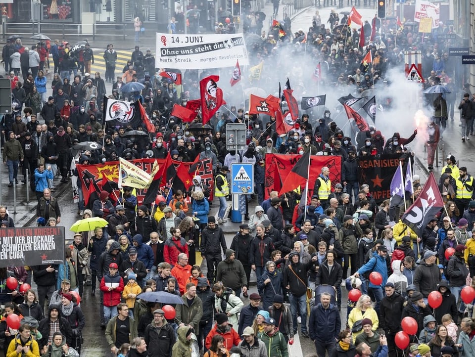 Blick auf einen Demonstrationsumzug auf einer Strasse in Zürich. Es gibt Leute mit Rauchfackeln.