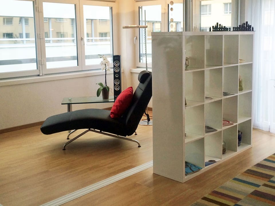 Ein moderner Sessel steht im Wohnbereich auf hellem Parkett, davor ein weisses, quadratisches Büchergestell.