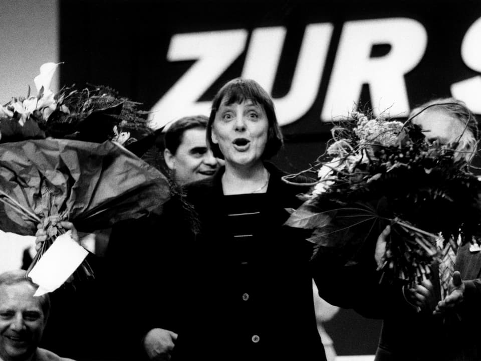 Angela Merkel mit einem Blumenstrauss in jeder Hand. 