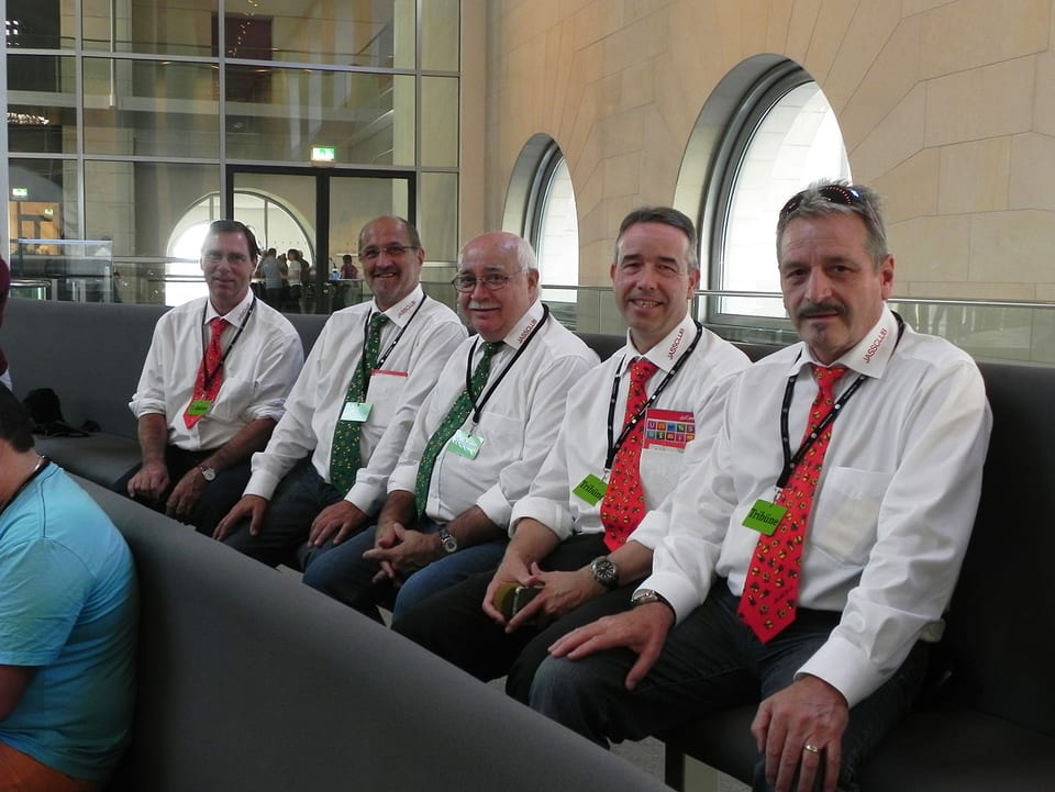 Fünf Männer mit weissem Hemd und Krawatte sitzen in einer Reihe.