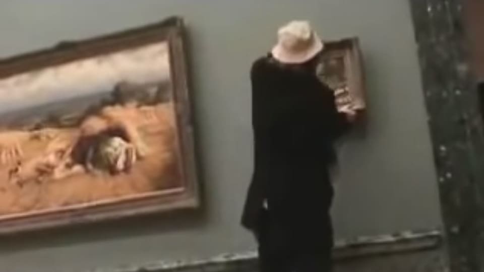 Ein Mann mit Hut hängt ein Bild im Museum auf. 