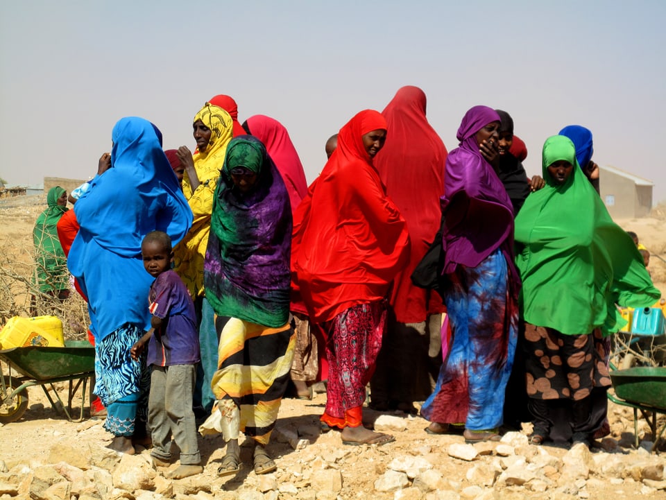 Frauen in bunten Gewändern warten in der Wüste.