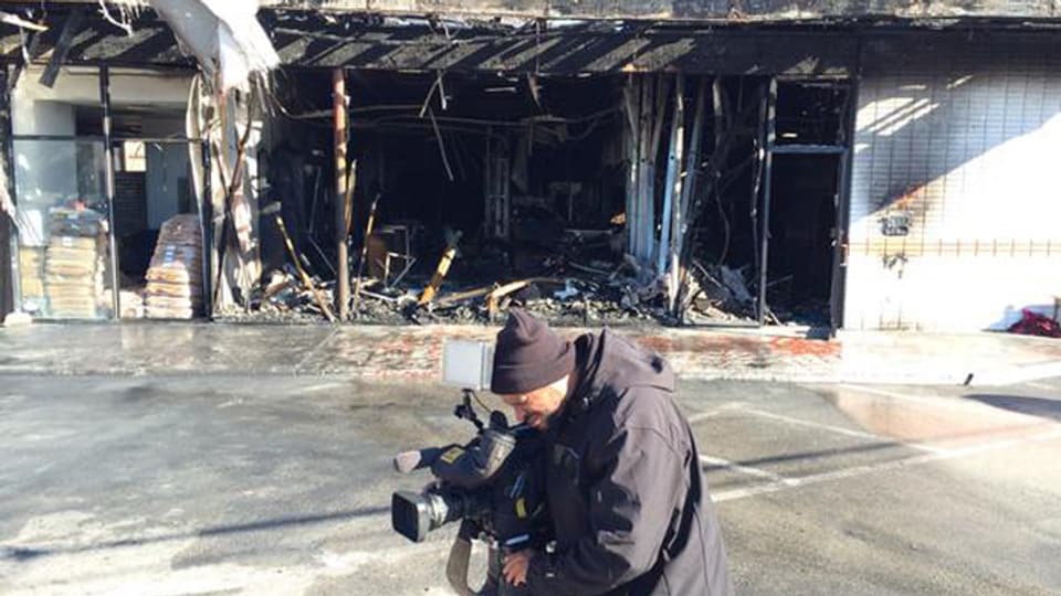 Ein Kameramann steht vor einem zerstörten Gebäude