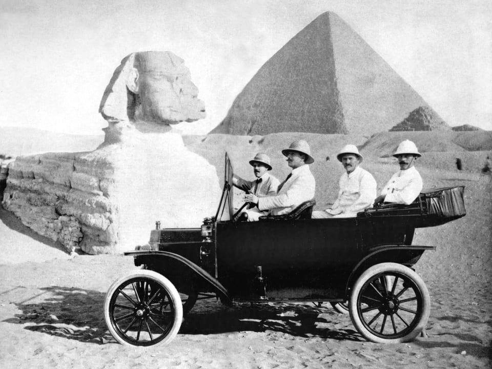 Vier Männer mit Schnauz und Tropenhelm in einem offenen Model T, im Hintergrund die Sphinx und die Cheops-Pyramide.
