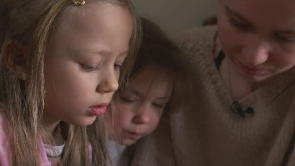 Anastasiia Yushchenko und ihre beiden Töchter betrachten in der Wohnung in Frutigen Familienbilder auf dem Handy.