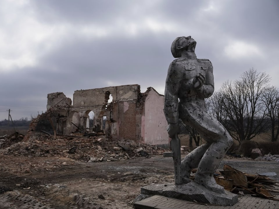 Eine sowjetische Statue steht vor einem komplett zerstörten Gebäude.