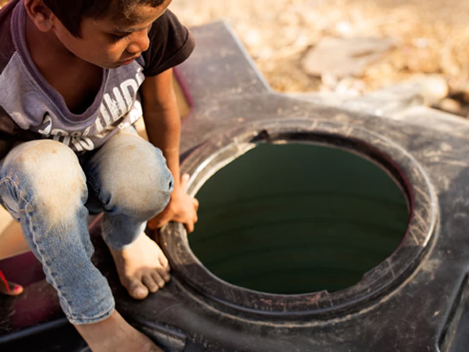 Ein Junge guckt von oben in einen vermutlich leeren Wassertank aus schwarzem Plastik.