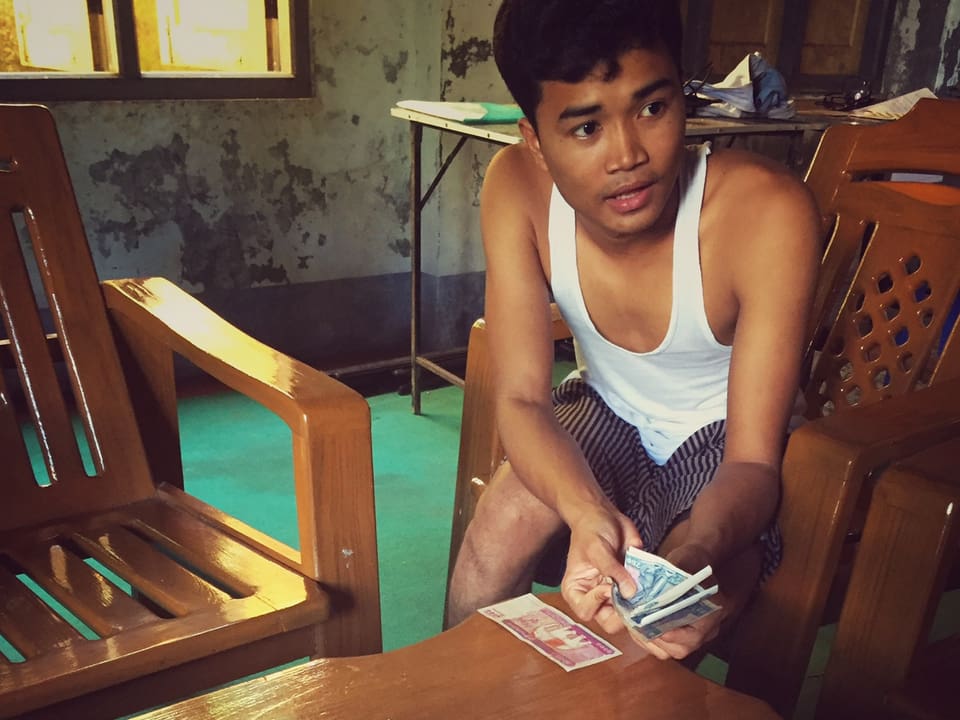 Ein junger Mann mit einem Geldbündel in der Hand sitzt an einem Tisch.