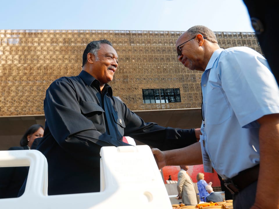Reverend Jesse Jackson schüttelt einem Mann die Hand, dahinter das Museumsgebäude