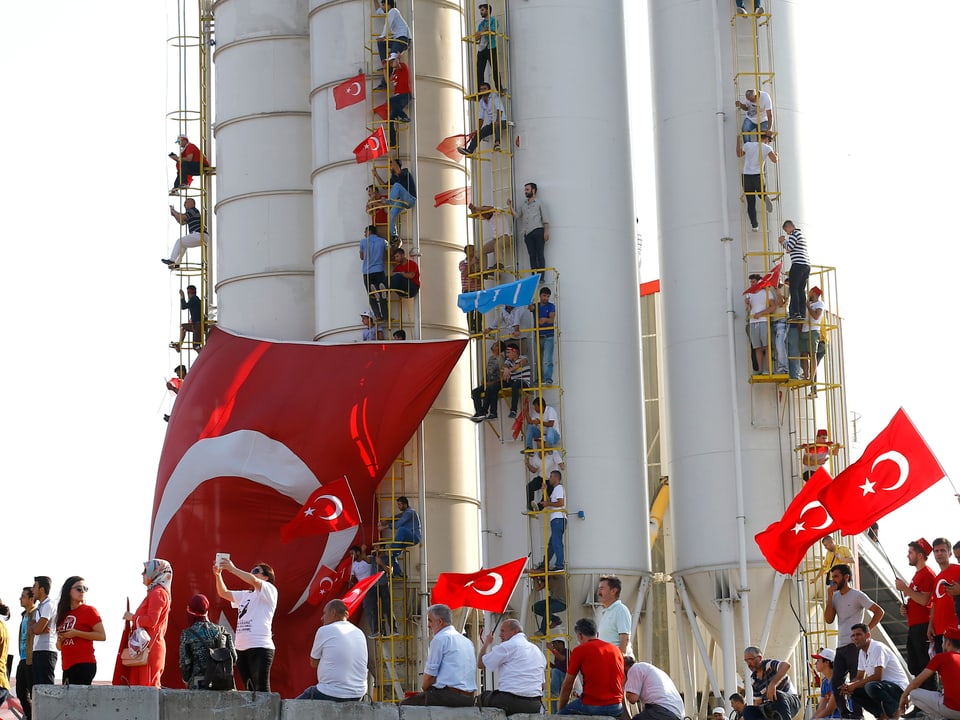 Menschen klettern auf Leitern an Türmen empor, viele schwenken Türkei-Flaggen.