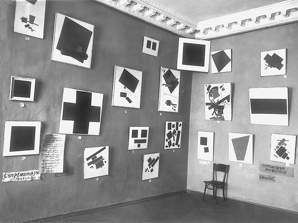 Schwarz-Weiss-Aufnahme: Zahlreiche abstrakte Gemälde in einem Ausstellungsraum. 