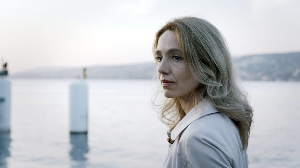 Eine blonde Frau steht am Ufer eines Sees.