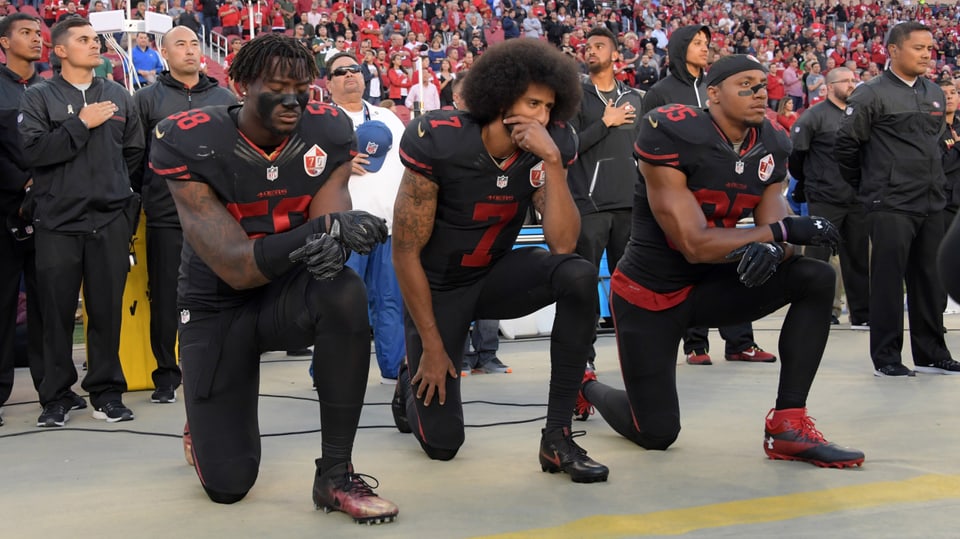 Die NFL-Spieler Eli Harold, Colin Kaepernick und Eric Reid von den San Francisco 49ers knien vor einem Spiel im Stadion.