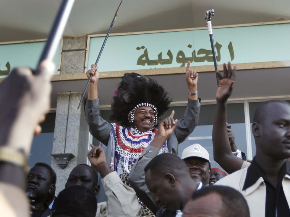 Omar al-Baschir in südsudanesischer Tracht mit Speer.