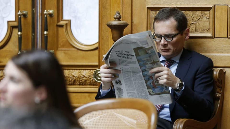 Köppel sitzt im Nationalrat und liest eine Zeitung.