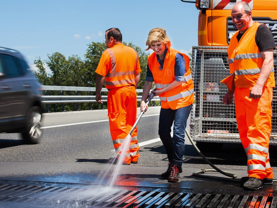Sabine Dahinden in oranger Weste putzt mit Wasserschlauch Belag auf der Autobahn