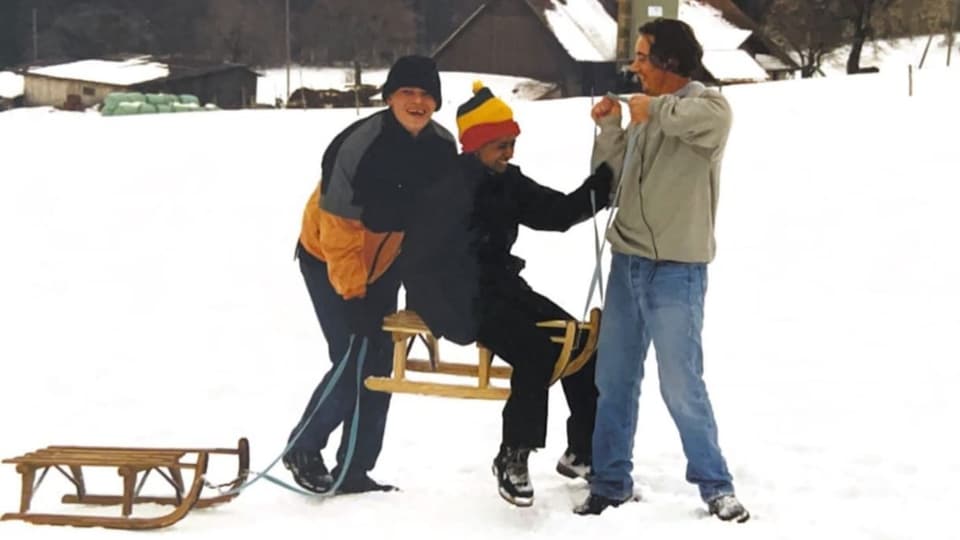 Drei junge Männer fahren Schlitten im Schnee und lachen.