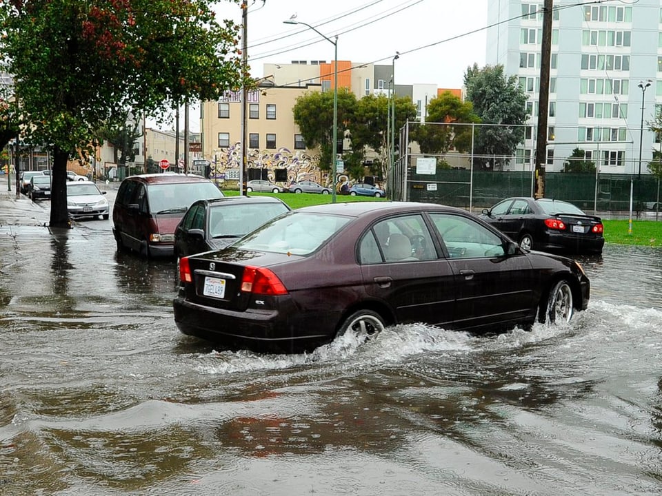 Ein Auto fährt auf überschwemmte Strassen.
