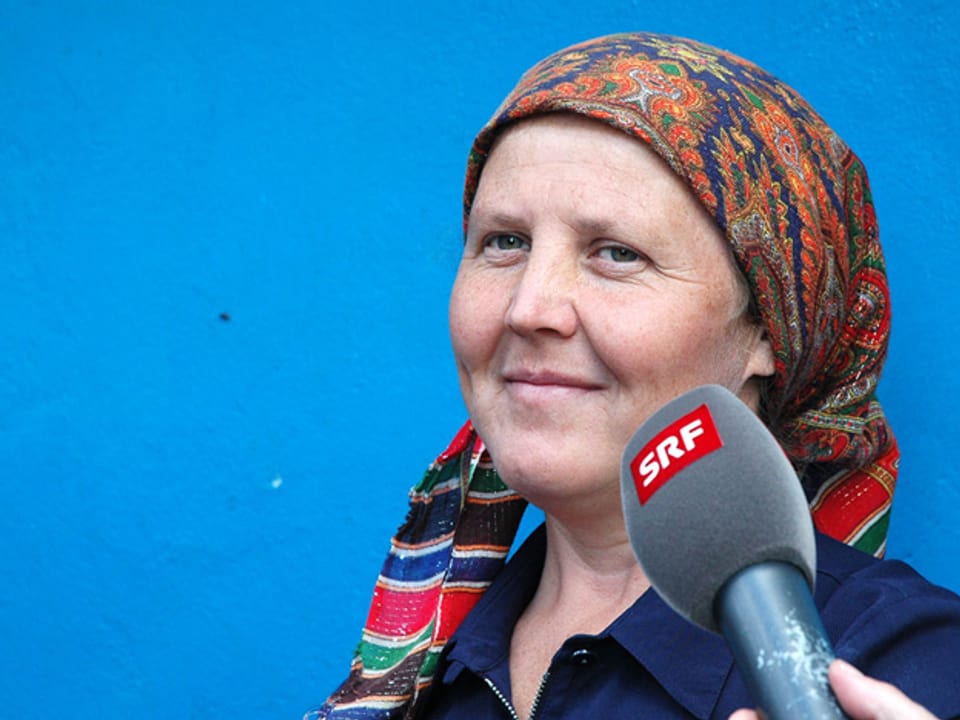 Porträtfoto von einer Frau mit Kopftuch vor einer blauen Wand.