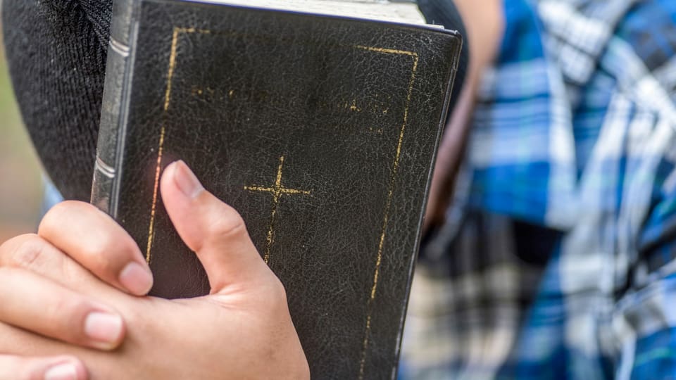 Ein Mann, der seinen Kopf nach unten hält, hat seine Hände auf einer schwarze Bibel.