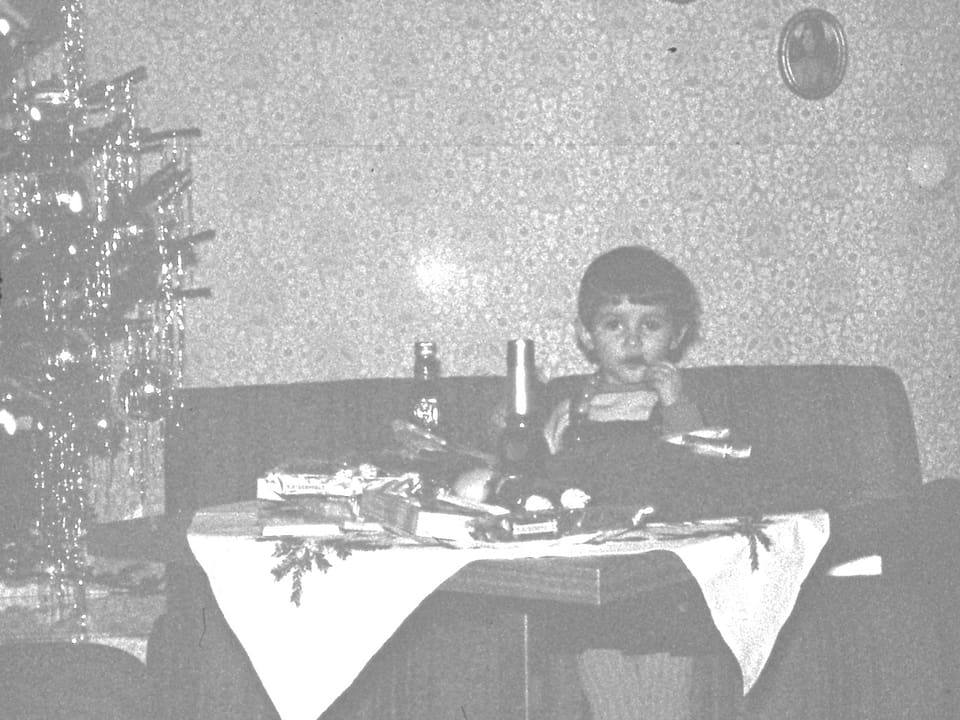 Kleines Mädchen sitzt neben einem mit Lametta geschmückten Weihnachtsbaum. (Schwarz-Weiss-Bild)