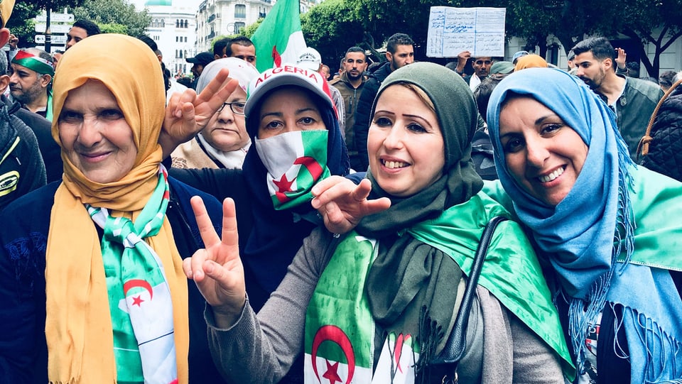 Vier Frauen mit Kopftuch und Algerien-Flagge auf der Strasse.