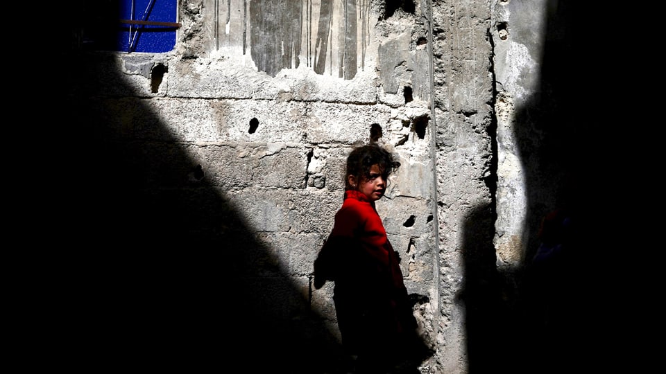 Ein Mädchen läuft in Palästina vor einer von Schüssen durchlöcherten Mauer vorüber.