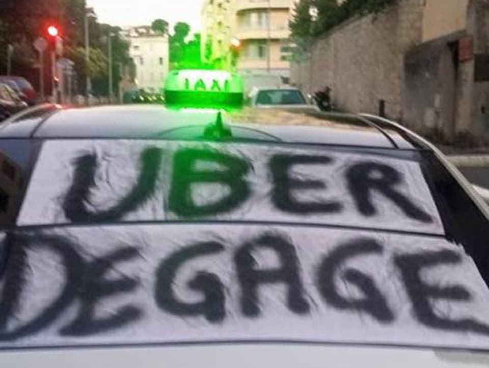 Bemaltes Leintuch auf Heckscheibe eines Taxis mit Schriftzug «Uber degage»