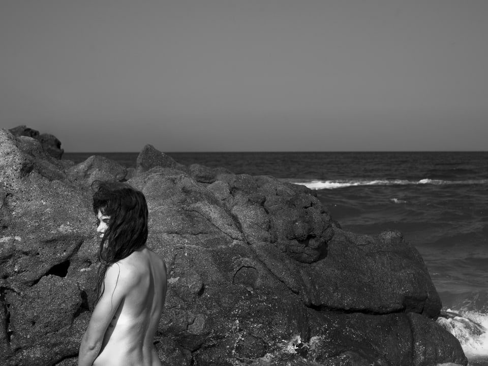 Eine nackte Frau steht vor dem Meer.