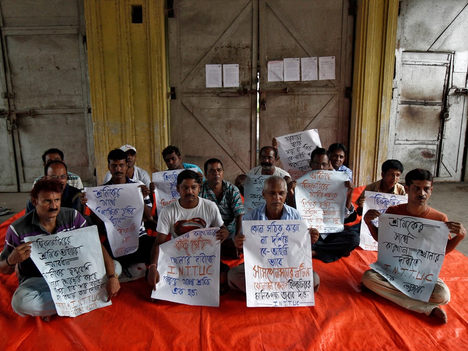 Arbeiter sitzen vor der Ambassador-Fabrik und halten Transparente hoch.
