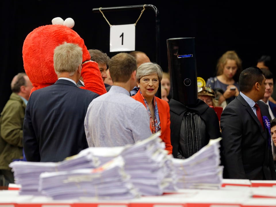 Theresa May im Wahllokal flankiert von den verkleideten Männern Lord Buckethead und Elmo