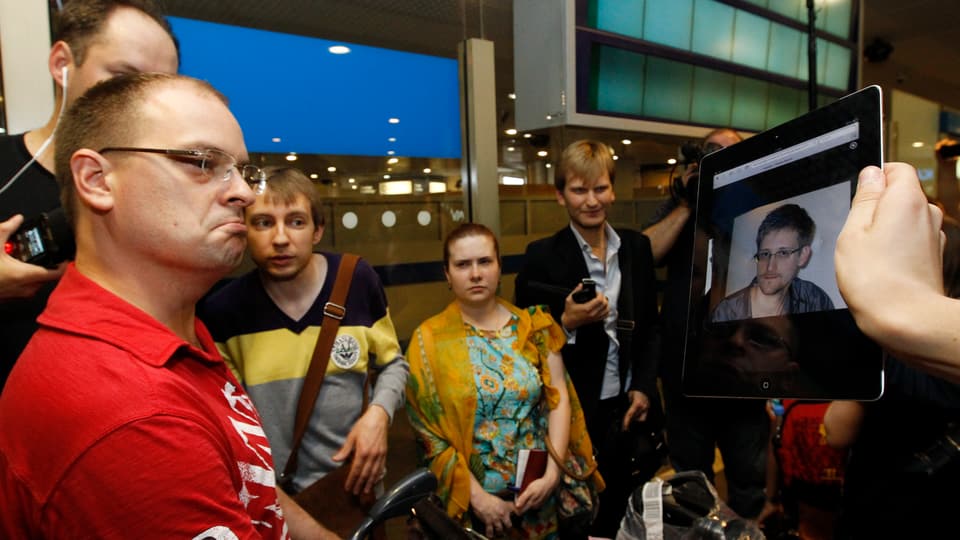Journalist zeigt Fluggästen auf eine iPad ein Bild von Edward Snowden.