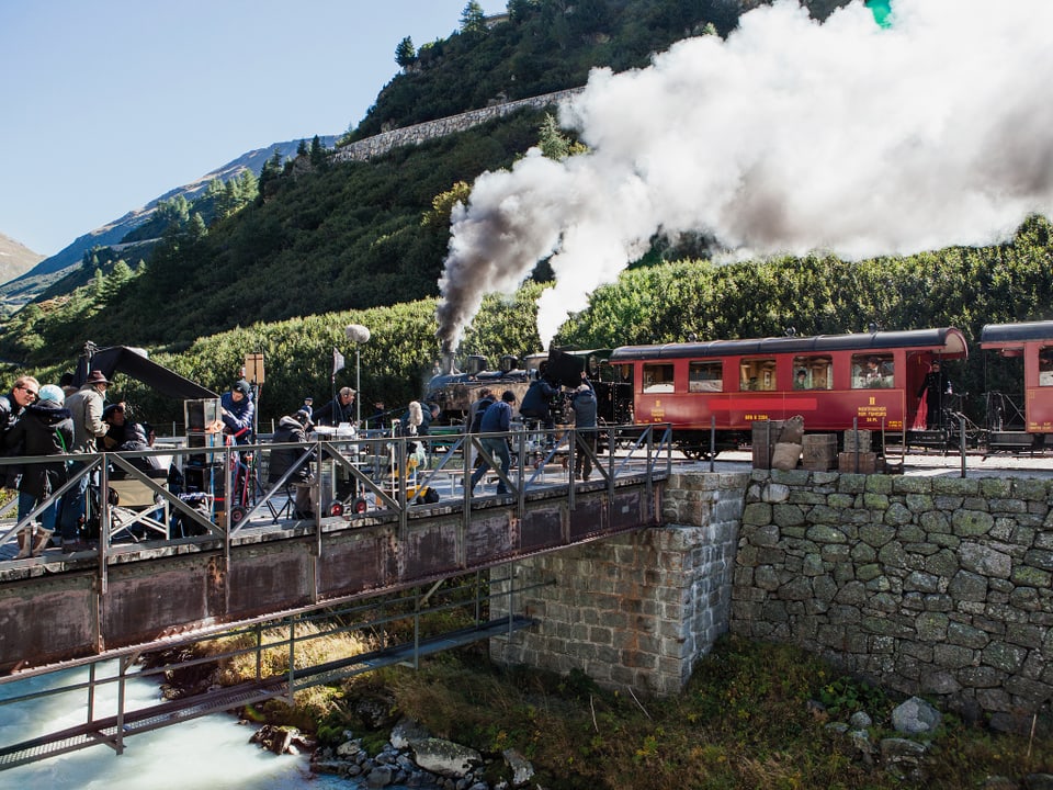 Ein historischer Zug, aus dessen Kamine es raucht und vor dem zahlreiche Menschen stehen.
