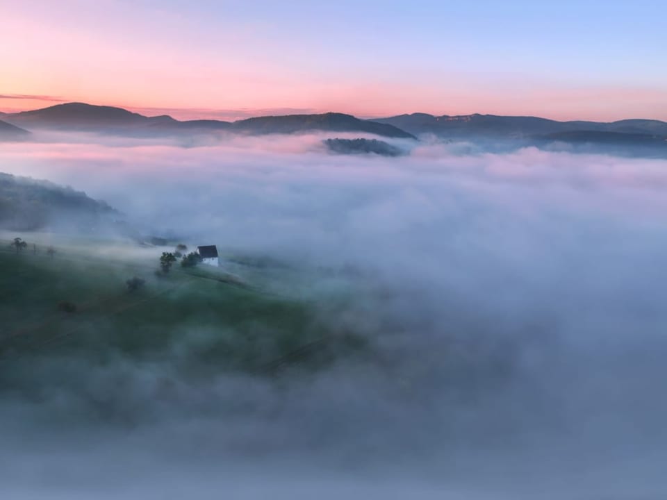 Viel Nebel, aber es ragen auch dunkle Hügel heraus in der Morgendämmerung