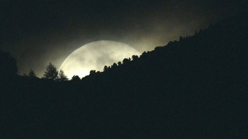 Der Vollmond geht hinter einem Berg auf.