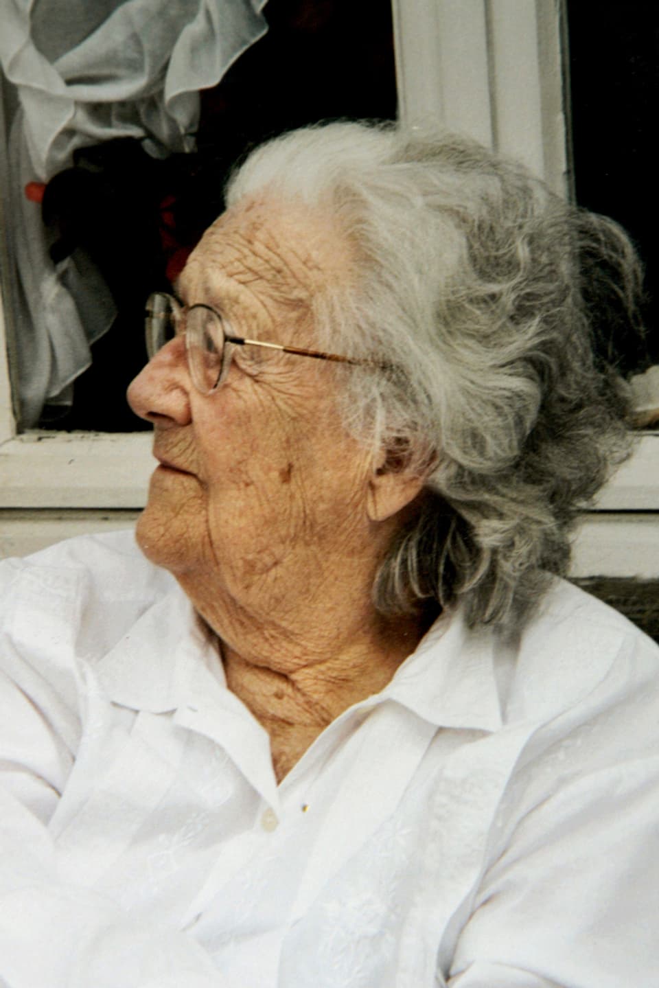 Eine ältere Frau mit Brille, zur Seite blickend.
